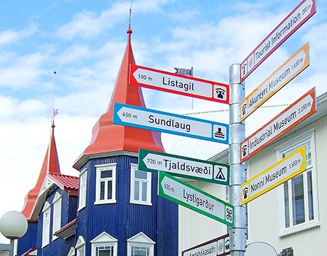 Colorful signpost pointing to local attractions in Akureyri, Iceland, with charming red-roofed buildings nearby | MSC Cruises Colorful signpost pointing to local attractions in Akureyri, Iceland, with charming red-roofed buildings nearby | MSC Cruises