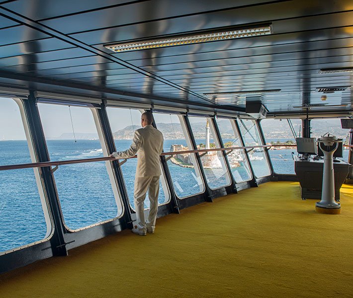 A person in a white suit enjoying panoramic sea views from a ship's bridge | MSC Cruises A person in a white suit enjoying panoramic sea views from a ship's bridge | MSC Cruises