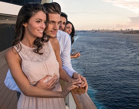 Couple enjoying ocean views from a cruise ship balcony with a city skyline in the distance | MSC Cruises Couple enjoying ocean views from a cruise ship balcony with a city skyline in the distance | MSC Cruises